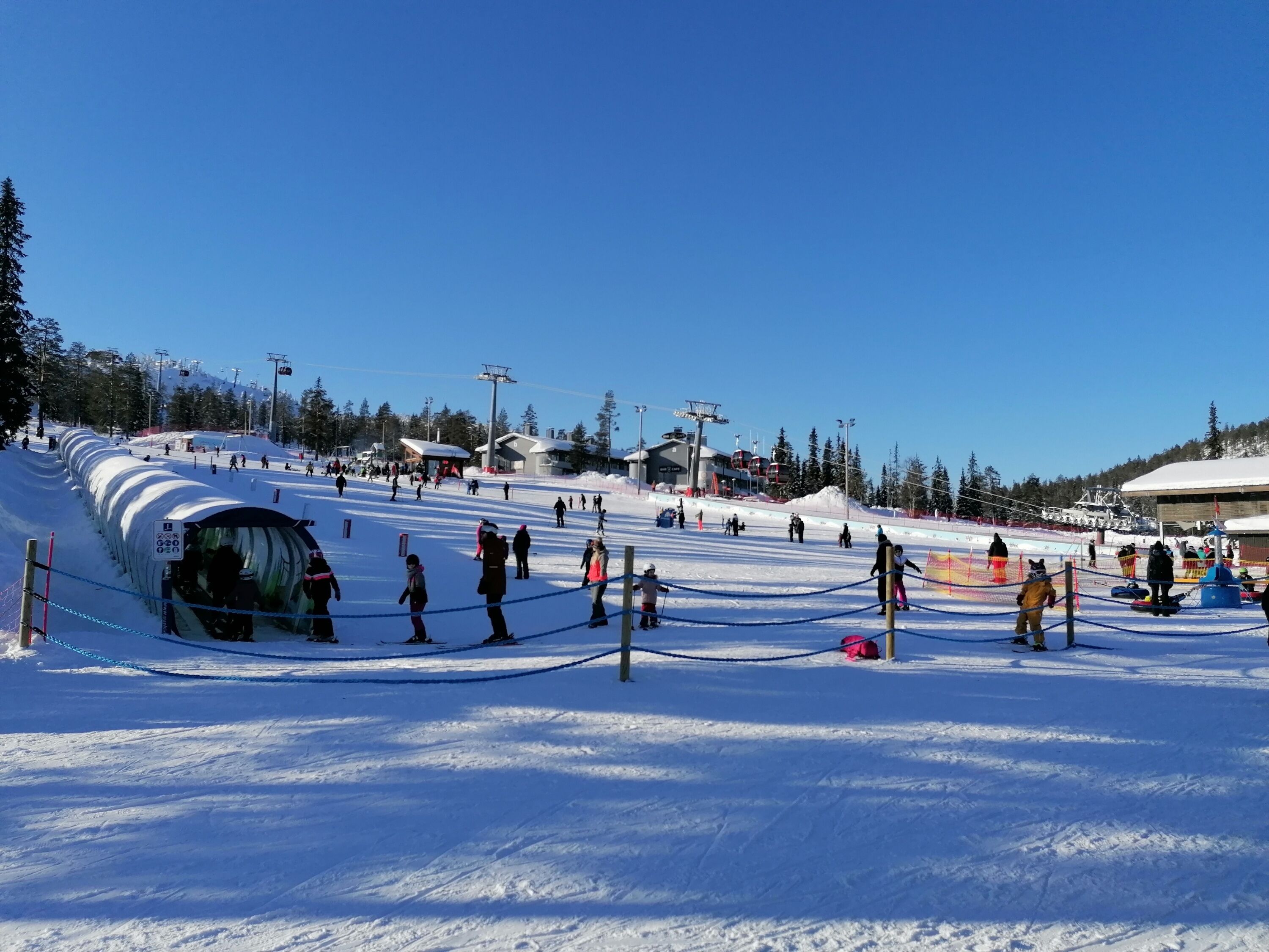 A ski resort with a snow-covered slope, ski lifts, and a clear blue sky.