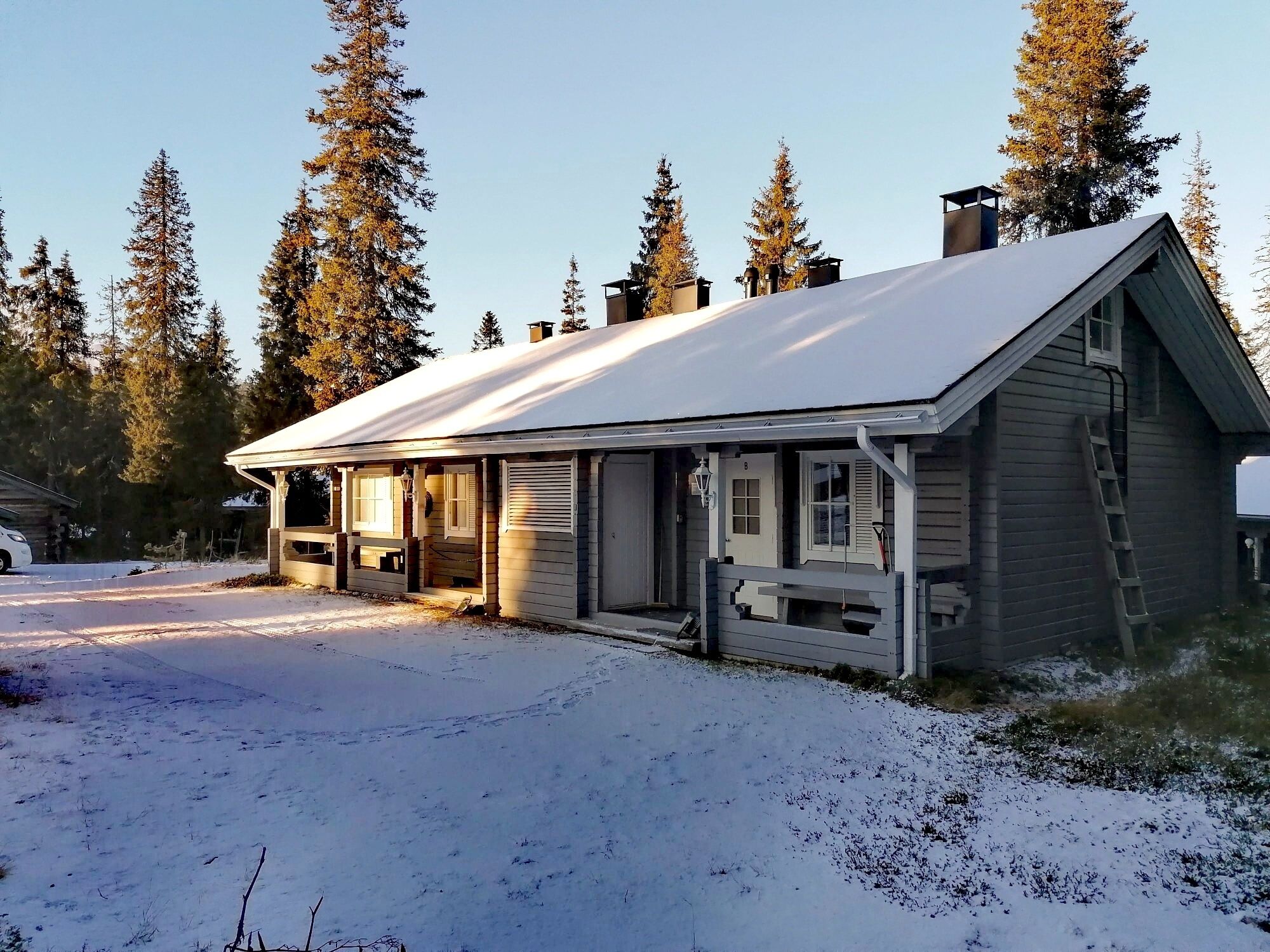 En stuga av trä med ett snötäckt tak, en veranda och en skorsten.