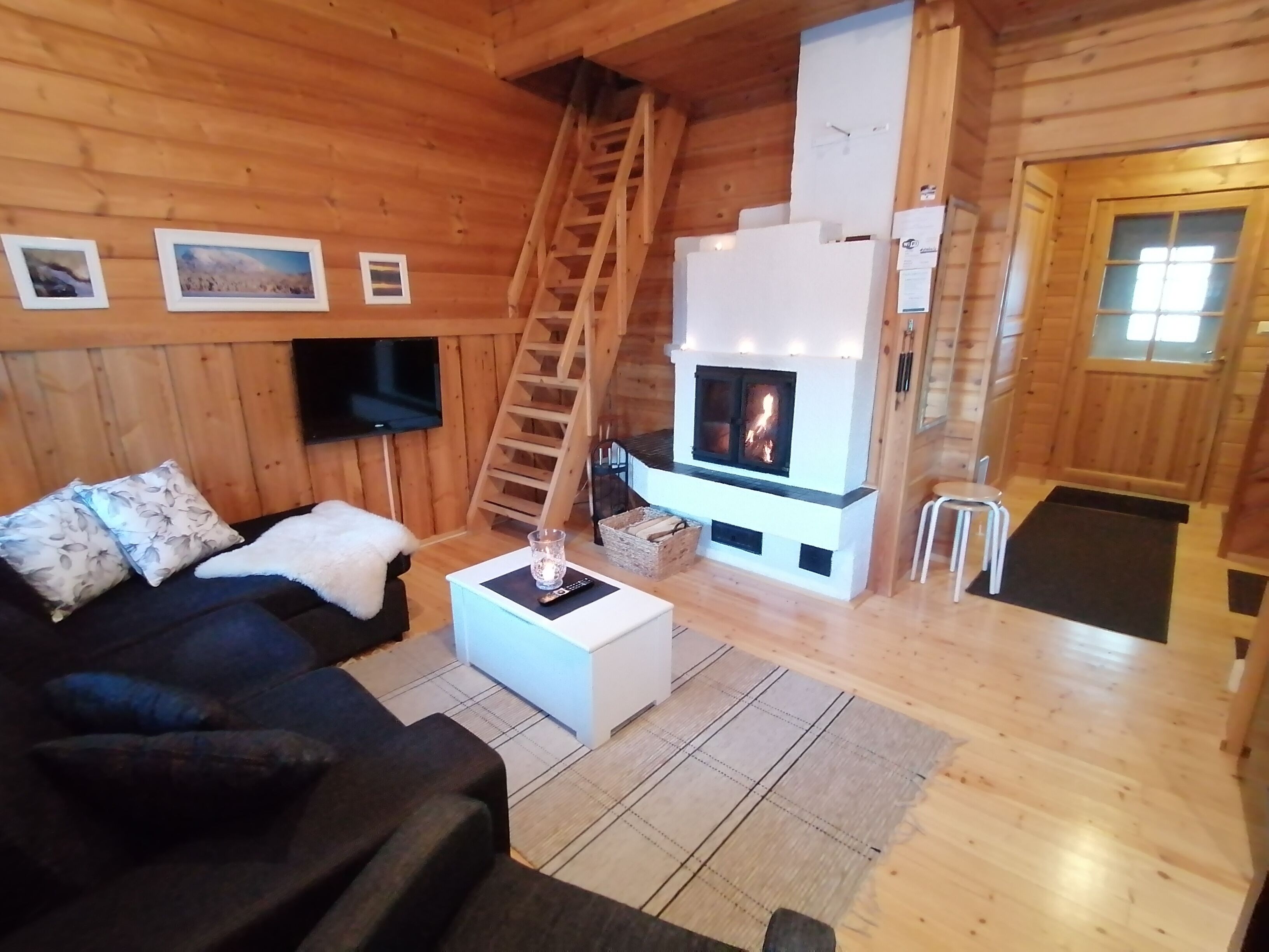 Accogliente interno di una baita in legno con camino, pareti in legno, un divano, un tavolino da caffè e una televisione.