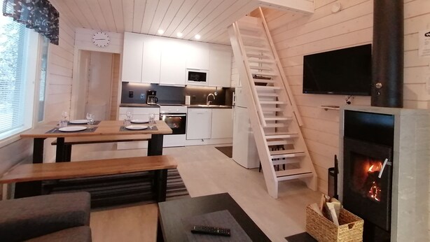 A compact kitchen with white cabinets, a microwave, and a stove. There is a wooden staircase leading to a loft area. - Rukantrio (Kuusamo)