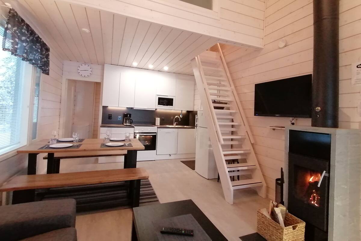Cocina compacta con gabinetes blancos, microondas y estufa. Una escalera de madera conduce a una zona en lo alto.