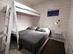 A bunk bed with a gray mattress and striped pillows, a small bedside table, and a wall-mounted lamp.