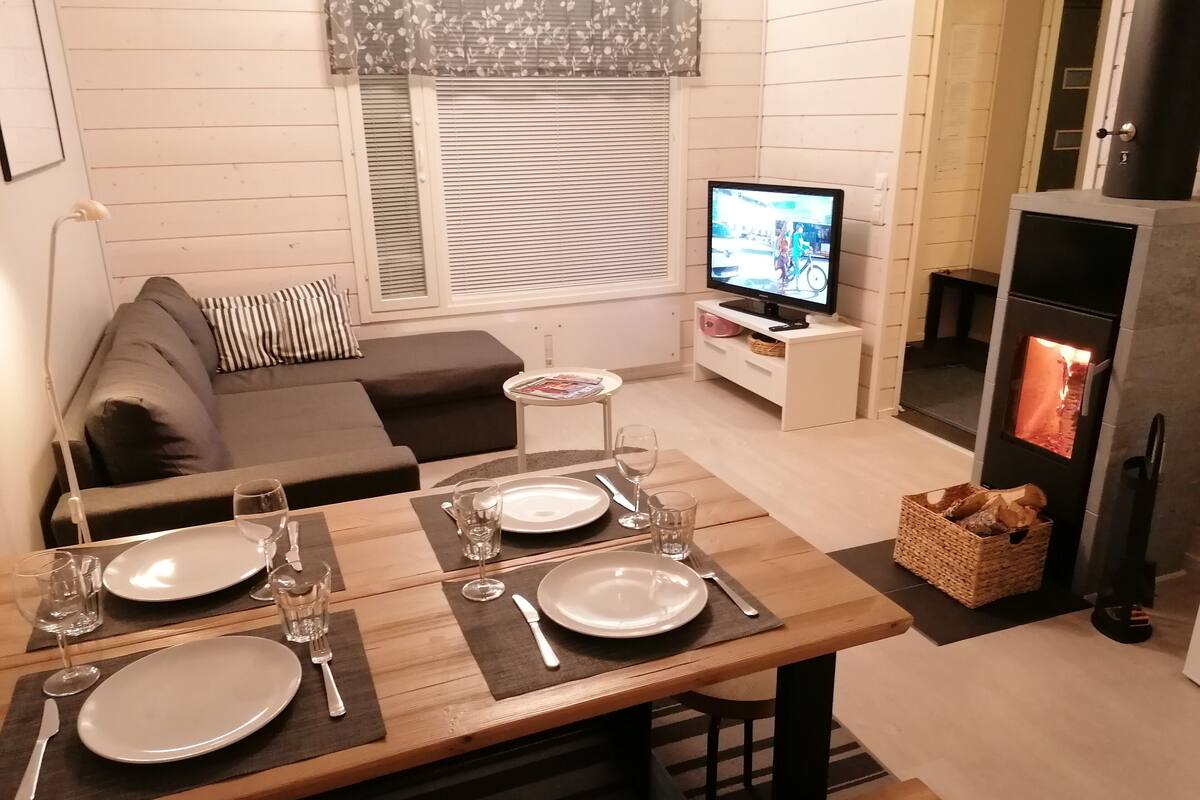 Una sala de estar acogedora con una mesa de comedor para dos personas, un sofá, un televisor y una estufa de leña.
