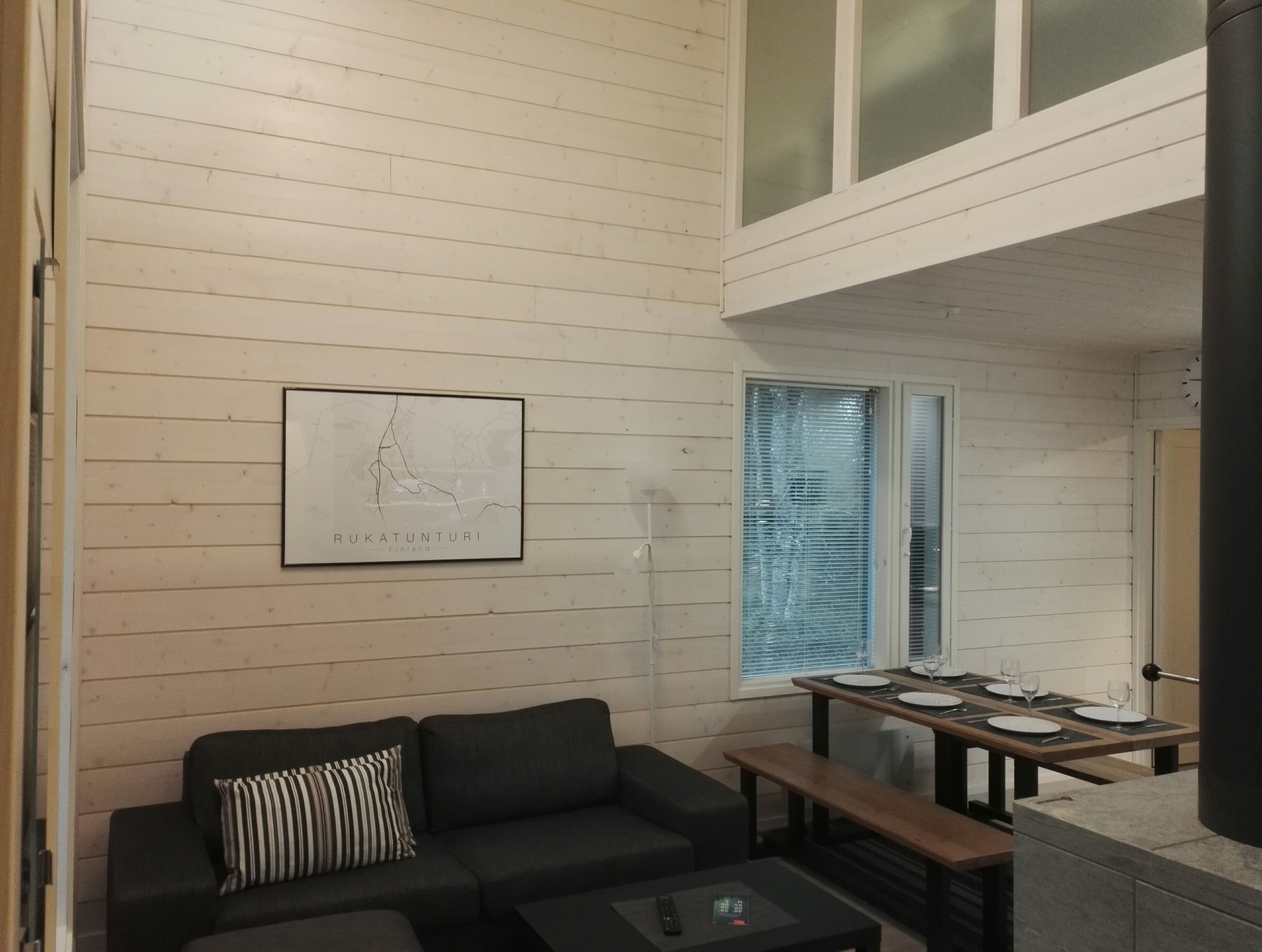 A modern interior with a black sofa, a dining table set for four, and a framed map on the wall.