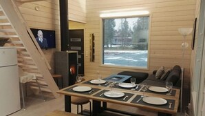 A compact living space with a dining area, a television, a window with a view of trees, and a staircase. - Rukantrio (Kuusamo)