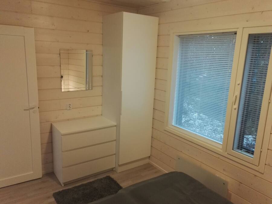 Una habitación con interior de madera, un armario, un espejo, una ventana con persianas y una alfombra pequeña.