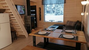 A cozy cabin interior with a dining table set for two, a kitchen area with a refrigerator, a fireplace, and a television mounted on the wall. - Rukantrio (Kuusamo)