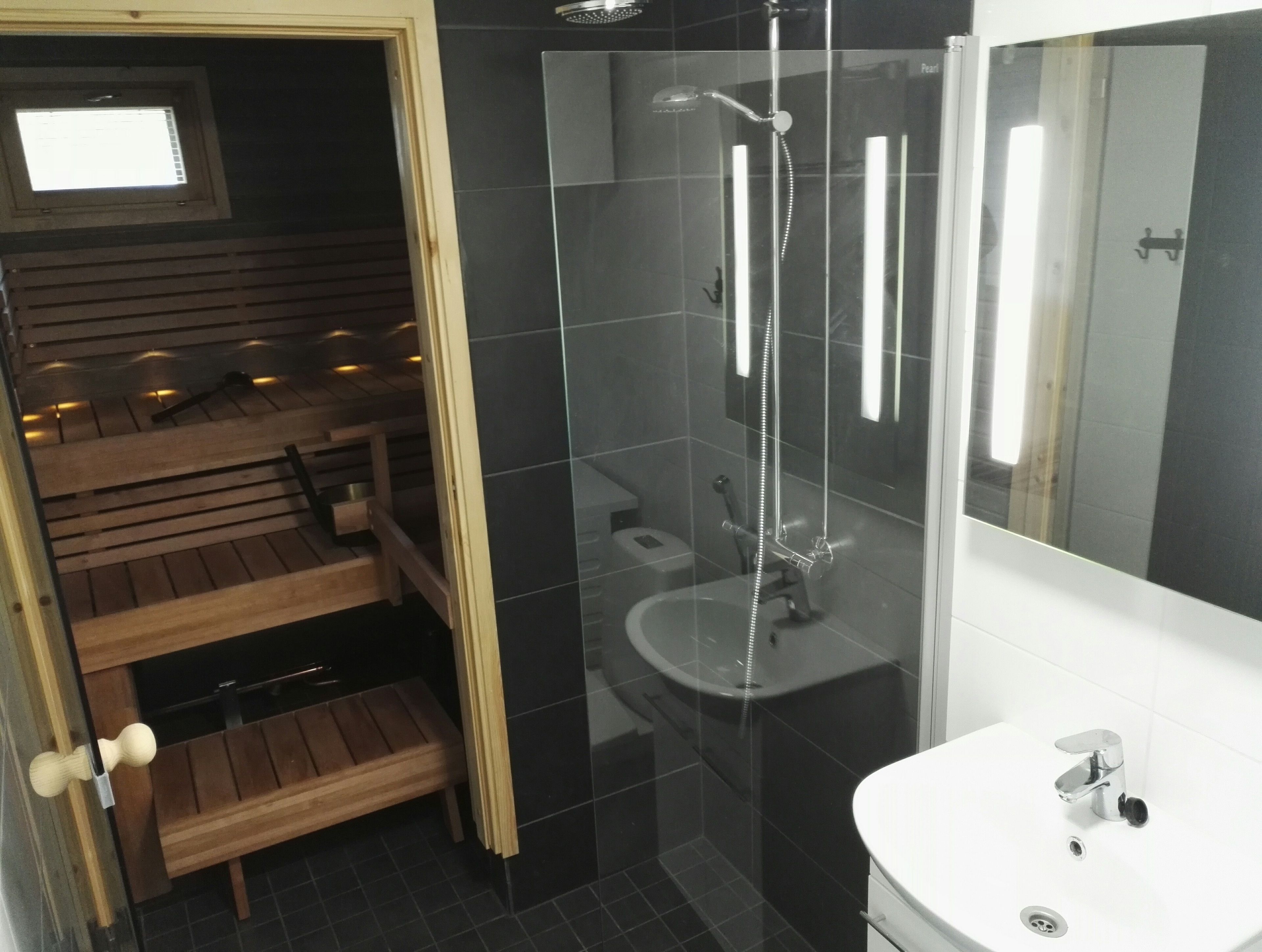 Un baño moderno con ducha envuelta en vidrio, un banco de madera y un lavamanos con espejo.