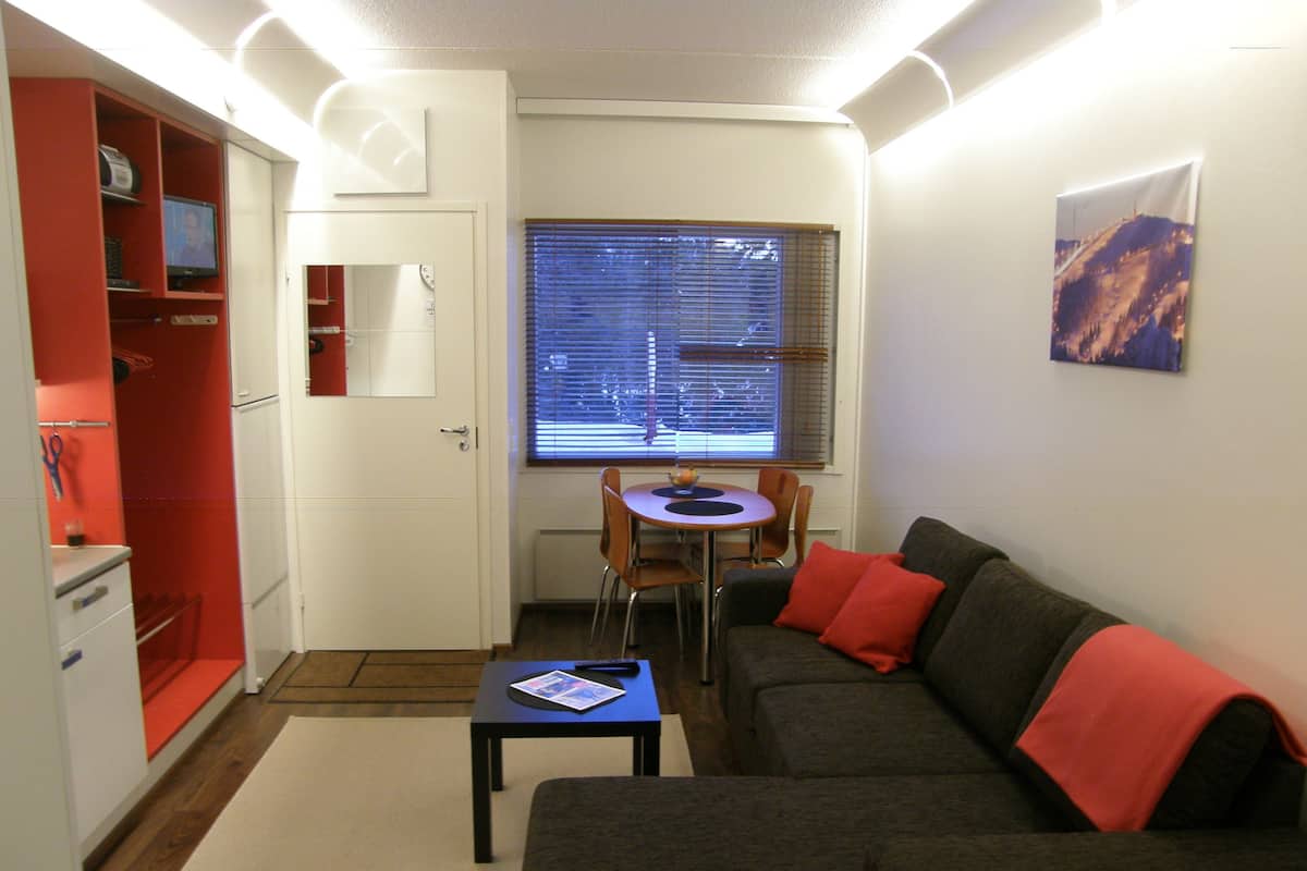 Un espace de vie compact comprenant un canapé, une petite table, un téléviseur et une fenêtre avec des stores.