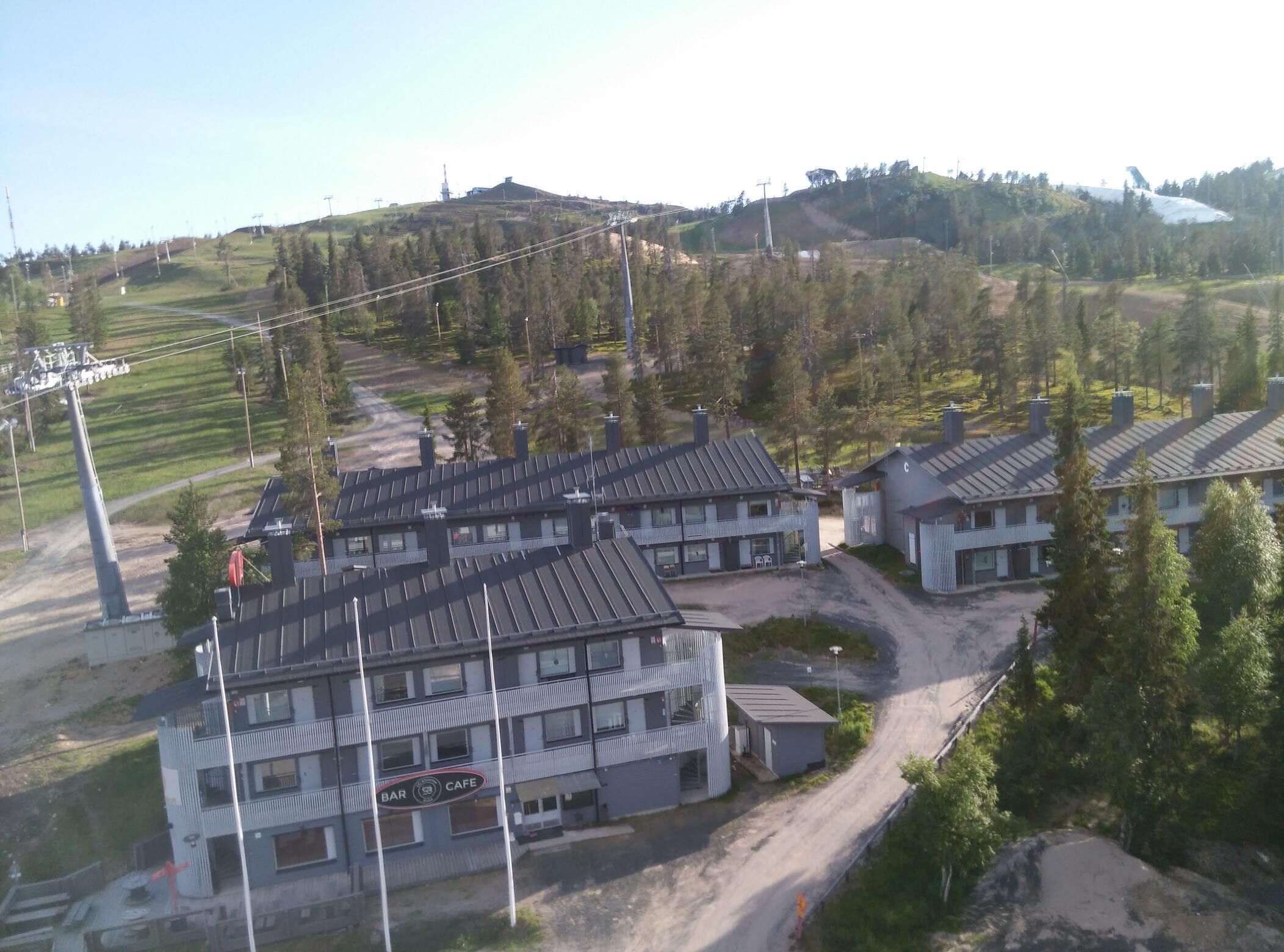 Ein modernes Gebäude mit Bar und Café im Erdgeschoss, umgeben von hügeliger Landschaft und Bäumen.