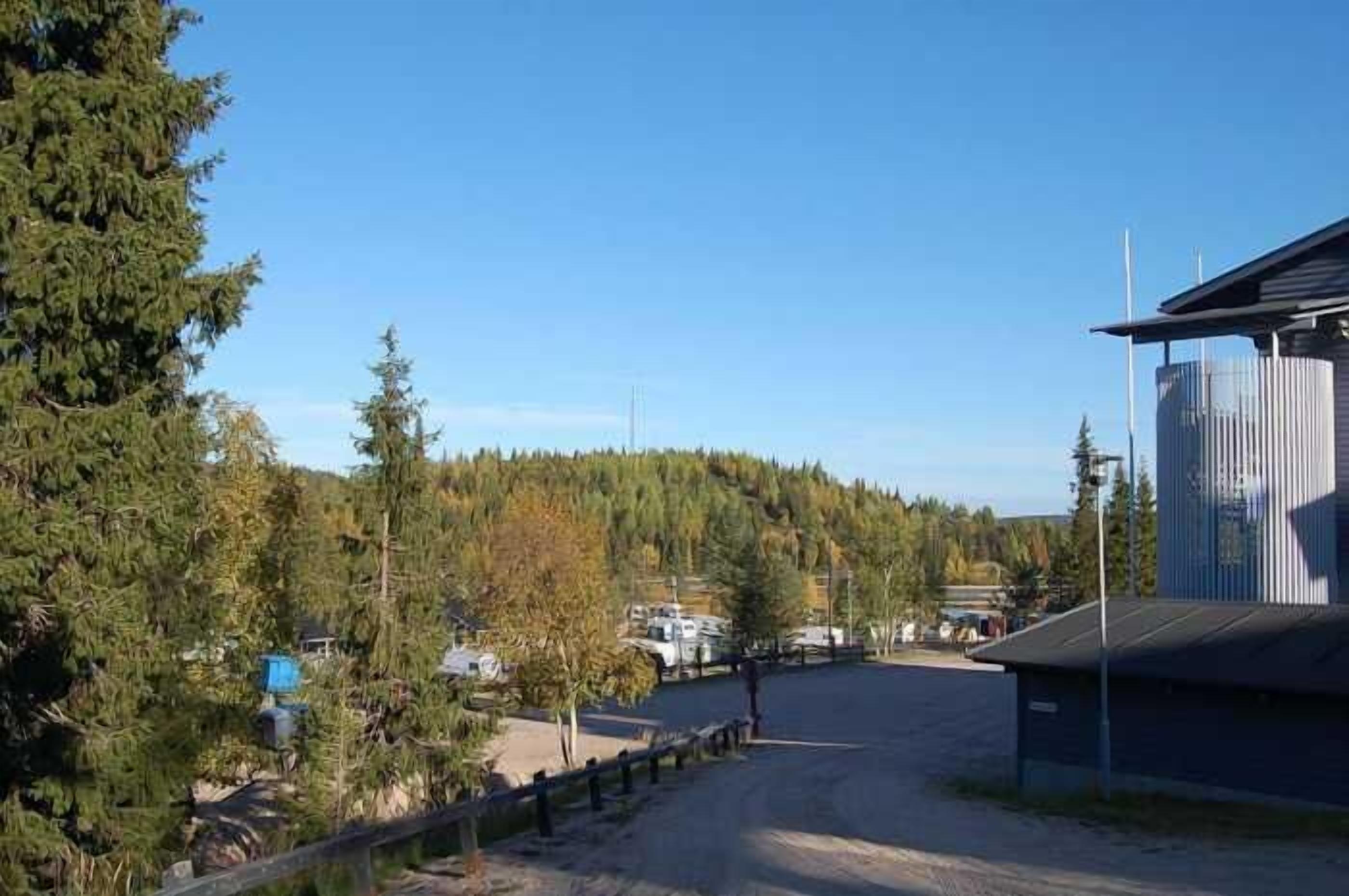 A rural road leading to a building with a silo, surrounded by trees and a clear sky.