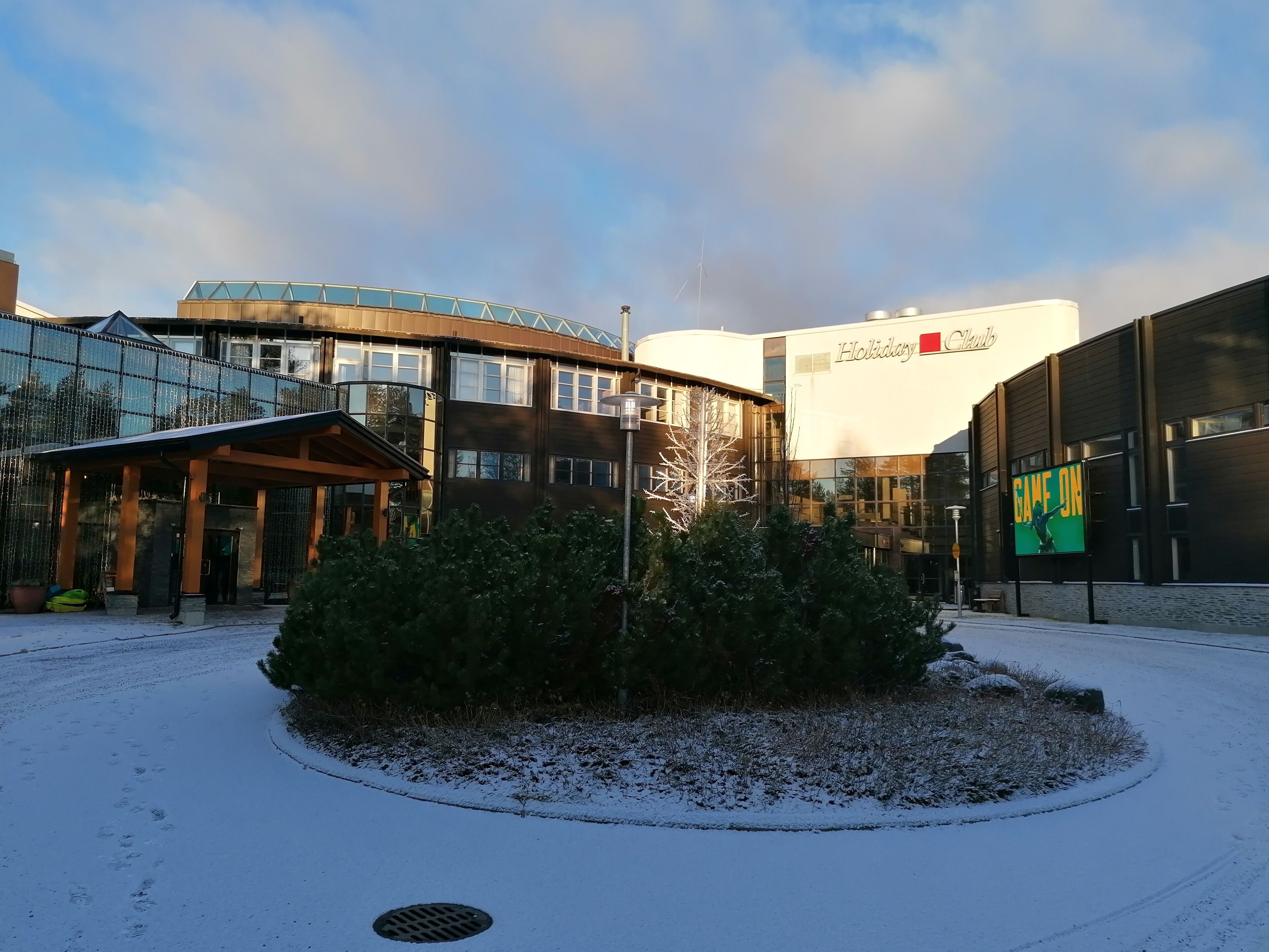 A hotel with a glass facade, a covered entrance, and a sign reading "Holiday Club".
