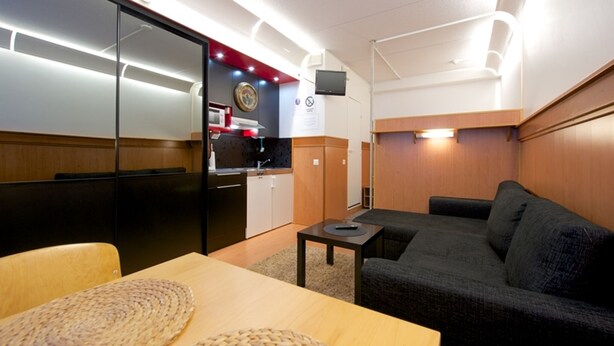 A compact room with a kitchenette, a sofa, a dining table, and a TV mounted on the wall. - Vuosselin Helmi (Kuusamo)