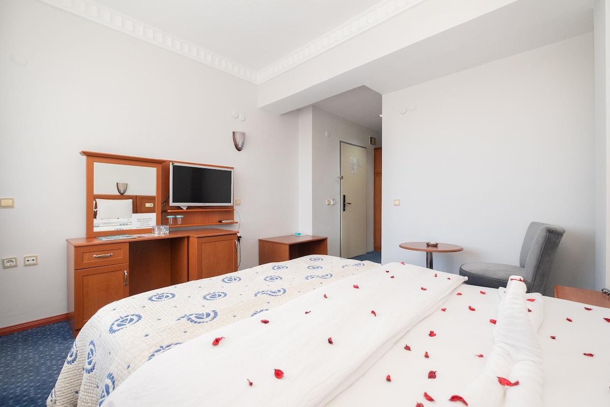 A hotel room with a bed, a desk, a chair, a television, and a door.