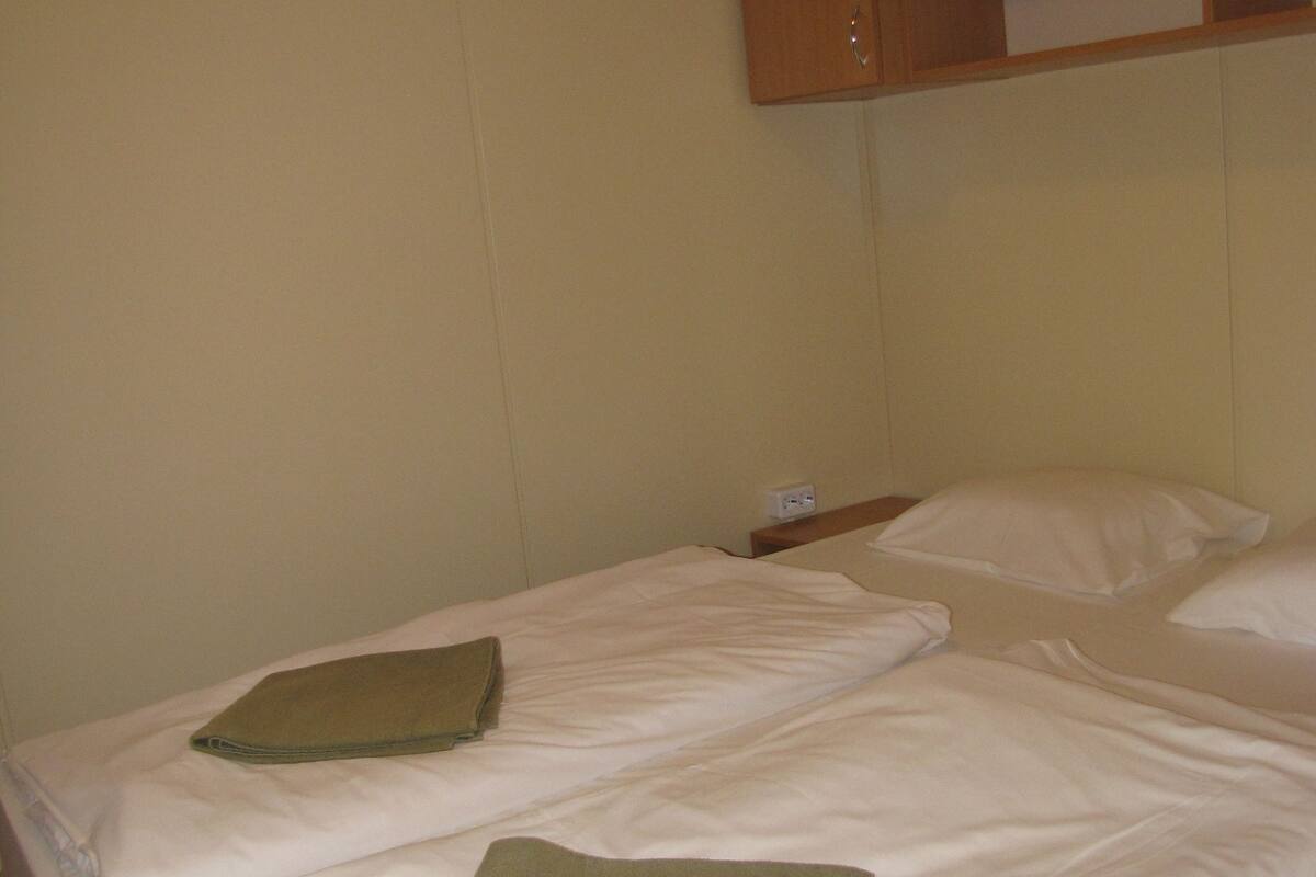 Un lit double avec du linge de lit blanc et deux serviettes vertes pliées.