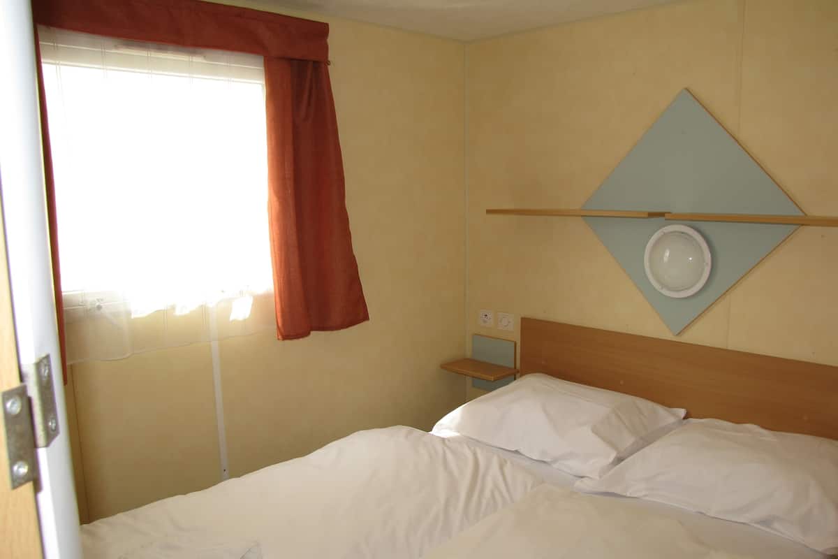Une chambre d’hôtel avec un lit, une table de chevet, une horloge murale et une fenêtre avec des rideaux.