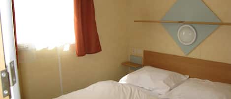 A hotel room with a bed, a nightstand, a wall clock, and a window with curtains.