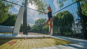 Een trampoline met veiligheidsnet, omringd door bomen en een heldere lucht.