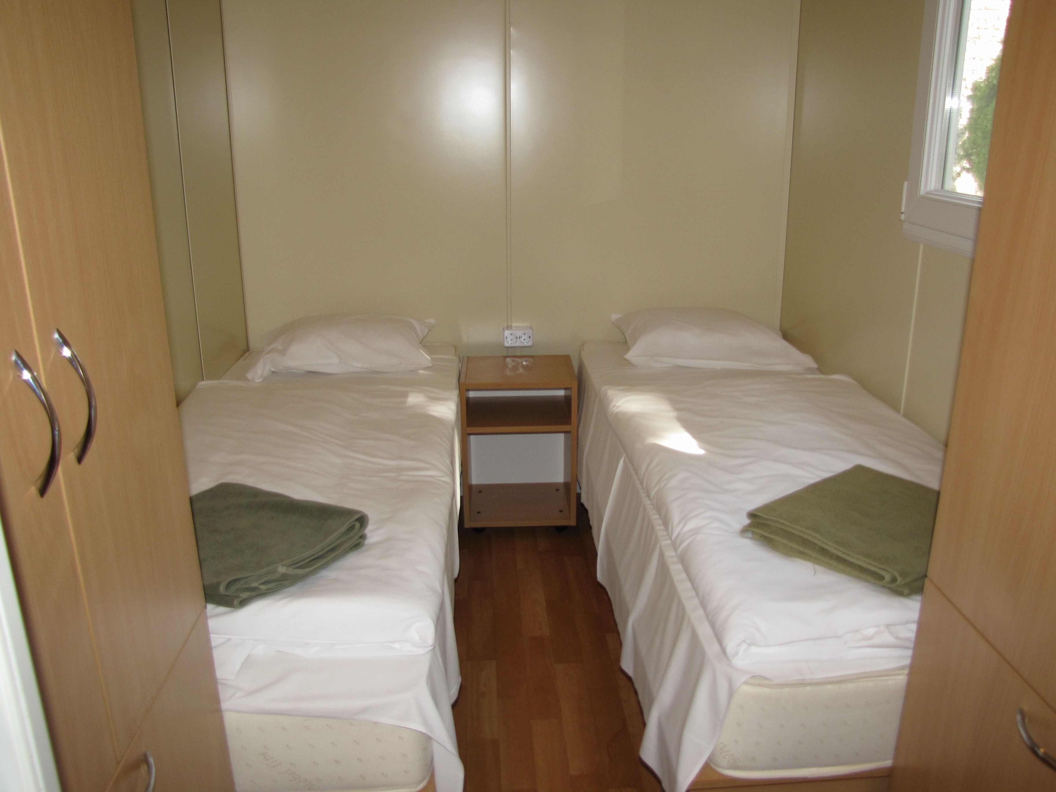 Un dormitorio pequeño y bien iluminado con dos camas, una mesita de noche y un ventanal.