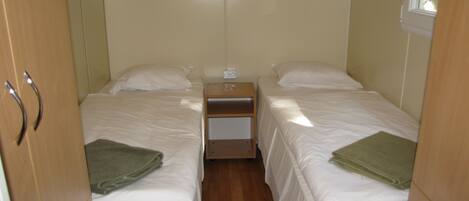 Un dormitorio pequeño y bien iluminado con dos camas, una mesita de noche y un ventanal.