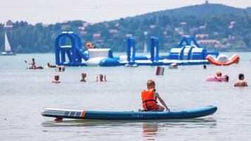 A person sitting on a blue inflatable raft in a body of water with inflatable structures in the background.