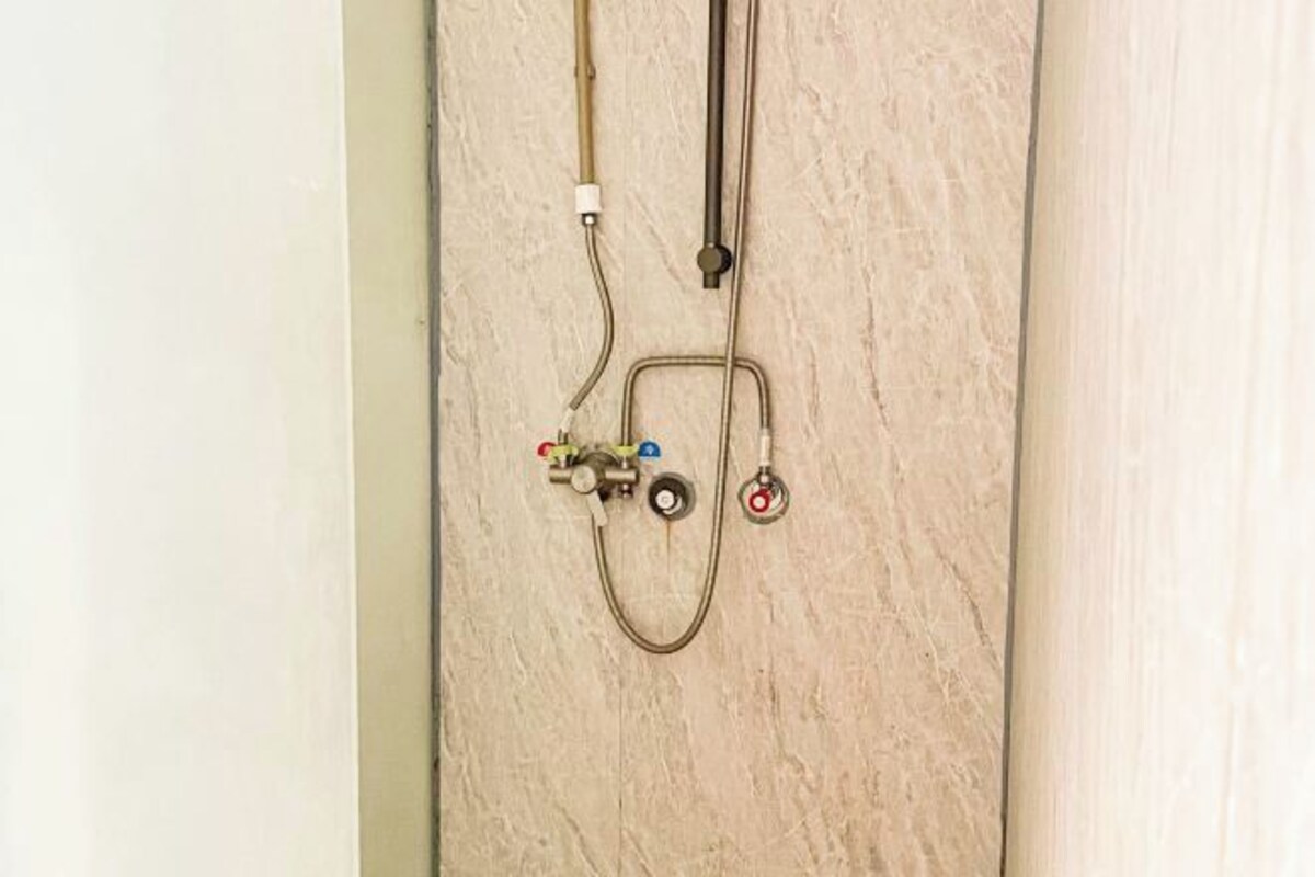 Un baño con pared de mármol, ducha y tuberías a la vista.