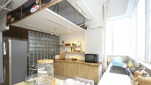 A modern kitchen with wooden cabinets, a large island with various kitchen items, a microwave, and a window providing natural light. - Phoenix Egg Youth Hostel (Zhuhai)