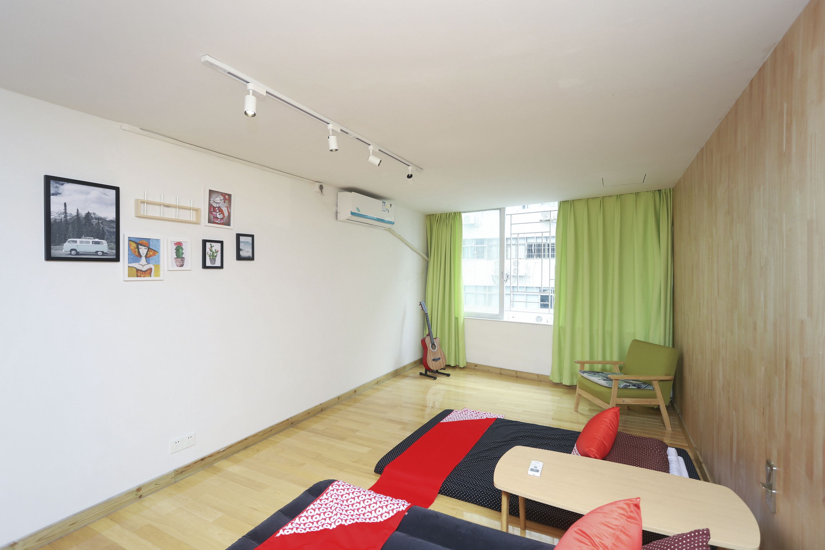 Een kamer met een bed, een stoel, een tafel en een gitaar. Er hangen foto’s aan de muur en er is een raam met gordijnen.