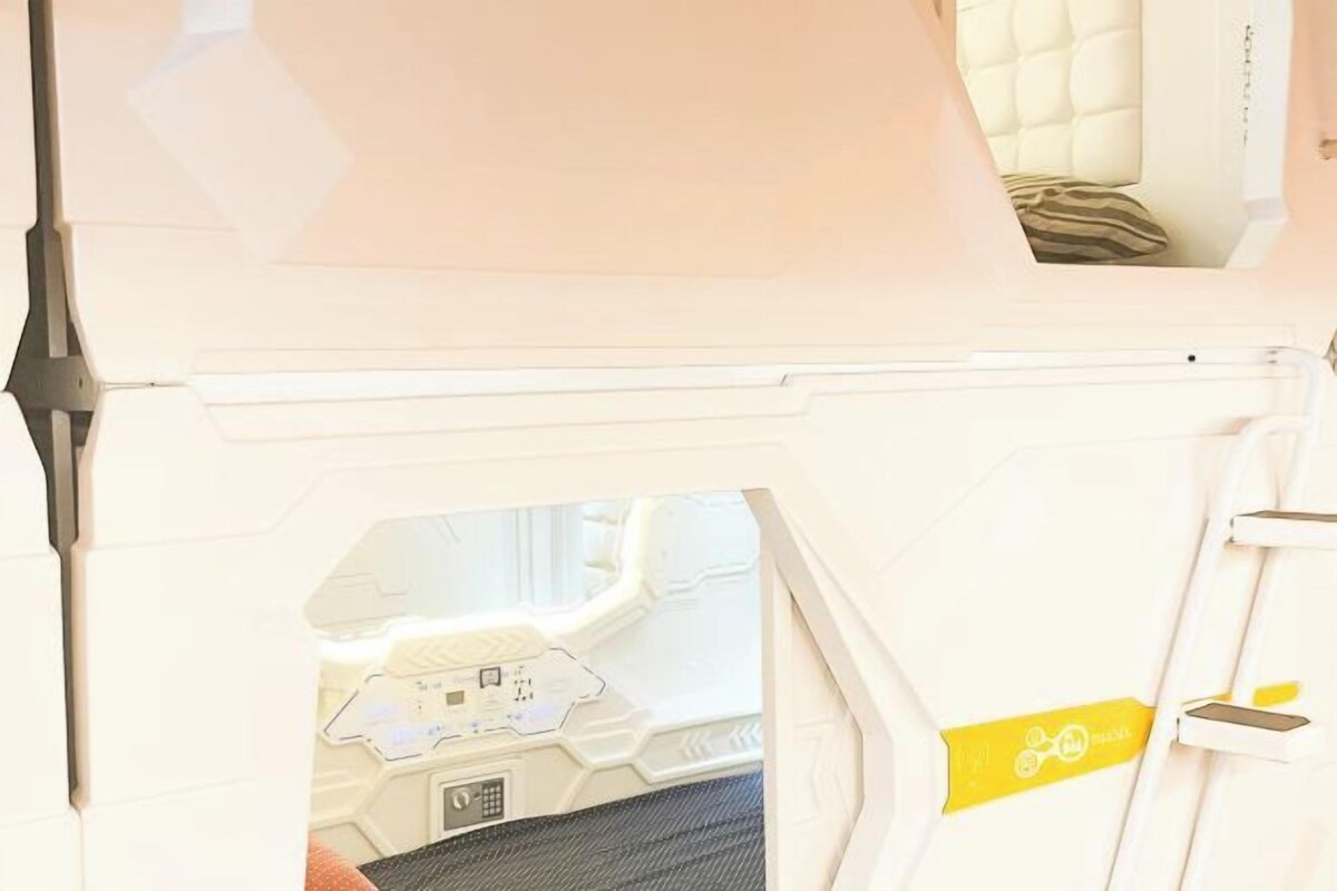 A white, futuristic-looking room with a control panel and a bed with a striped pillow.