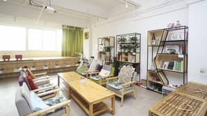 A well-lit room with a long table, several chairs, and bookshelves filled with books and plants. - Phoenix Egg Youth Hostel (Zhuhai)