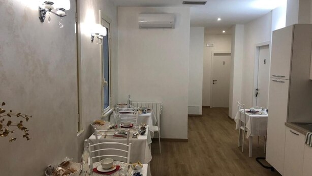 A dining area with white tables and chairs, a kitchen area with a refrigerator, and an air conditioning unit on the wall.