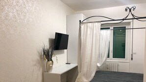 A bedroom with a bed, a desk, a TV, and a window with curtains.