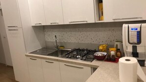 A compact kitchen with white cabinets, a gas stove, a sink, and a coffee machine.
