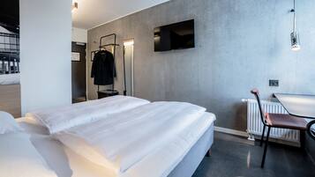 Una habitación de hotel moderna con una cama grande, un escritorio, una silla, un televisor y un perchero.
