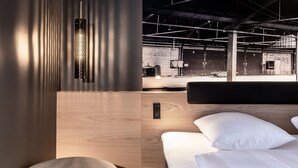Una habitación de hotel moderna con cabecera de madera, una mesita de noche y una lámpara colgante.