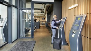 Un moderno vestíbulo de hotel con un mostrador de recepción, un quiosco digital informativo y una pared de madera.