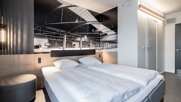 A modern hotel room with a large bed, a seating area, and a view of the hotel's interior.