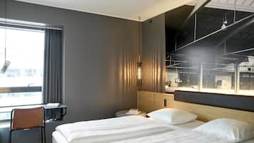 Una habitación de hotel moderna con una cama grande, un escritorio y vistas a una zona industrial.