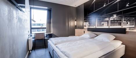 A modern hotel room with a large bed, a desk, and a view of the city.