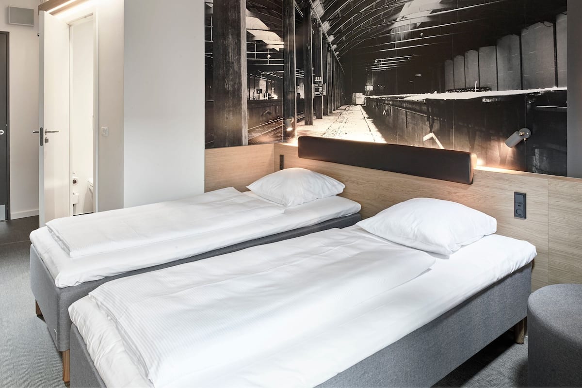 Ein Hotelzimmer mit zwei Einzelbetten, einem Holzkopfende und einem großen Wandbild einer Bahnhöfe.