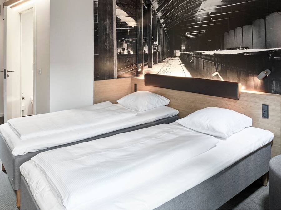 A hotel room with two single beds, a wooden headboard, and a large mural of a train station.