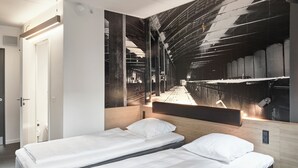 A hotel room with two single beds, a large mirror, and a view of a bridge.
