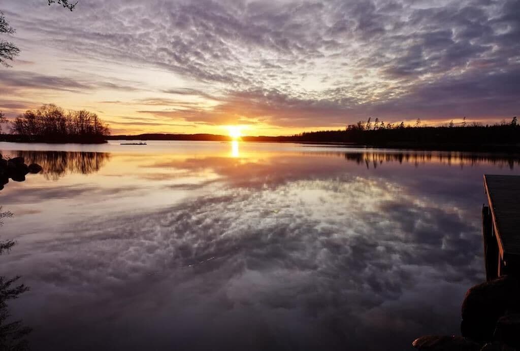 Un lago tranquilo al atardecer con un muelle a la derecha.