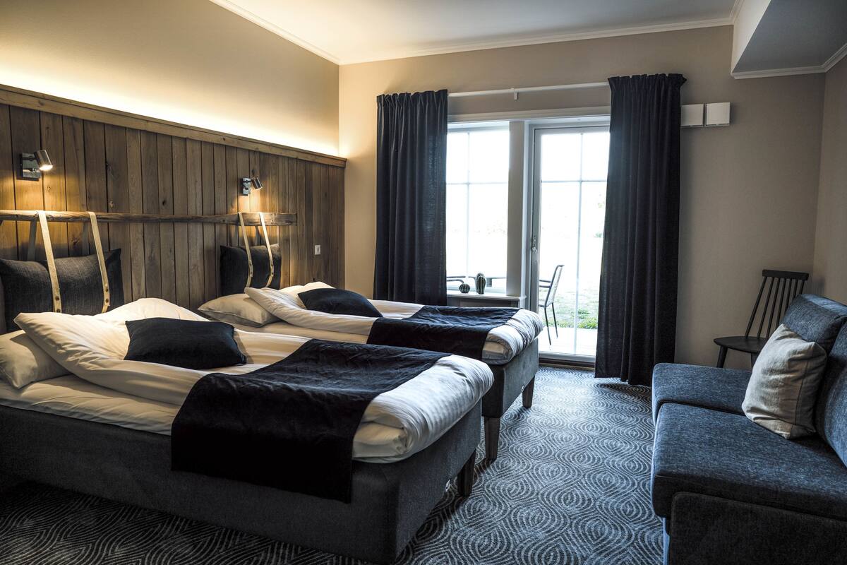 A hotel room with two beds, a sofa, and a balcony with curtains.