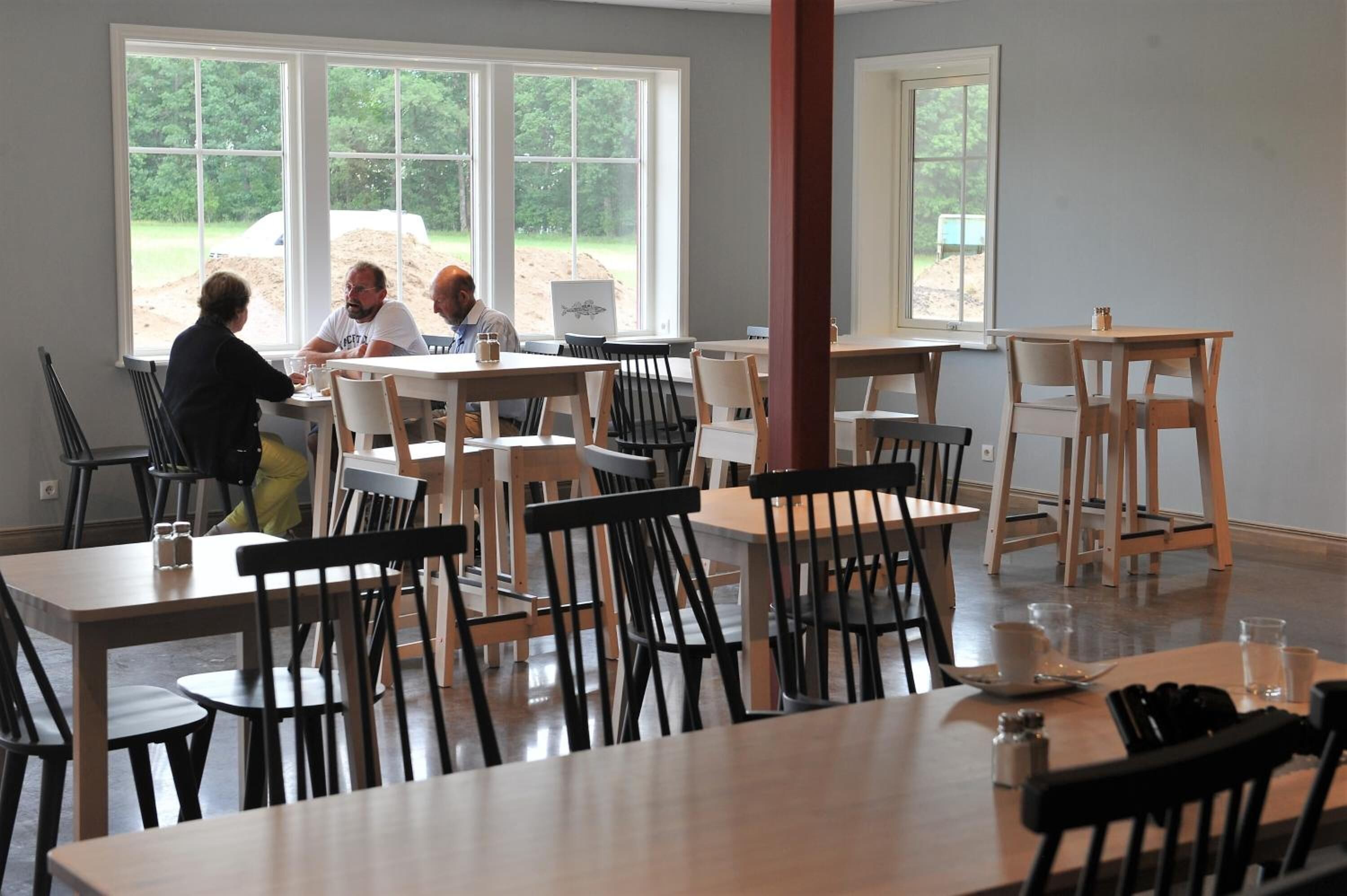A dining area with tables and chairs, large windows with a view of the outdoors, and a casual atmosphere.