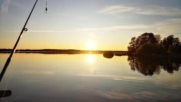 En fiskestang i stille vand med solnedgang i baggrunden.