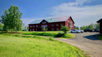 A large red building with a metal roof, surrounded by green fields and trees.