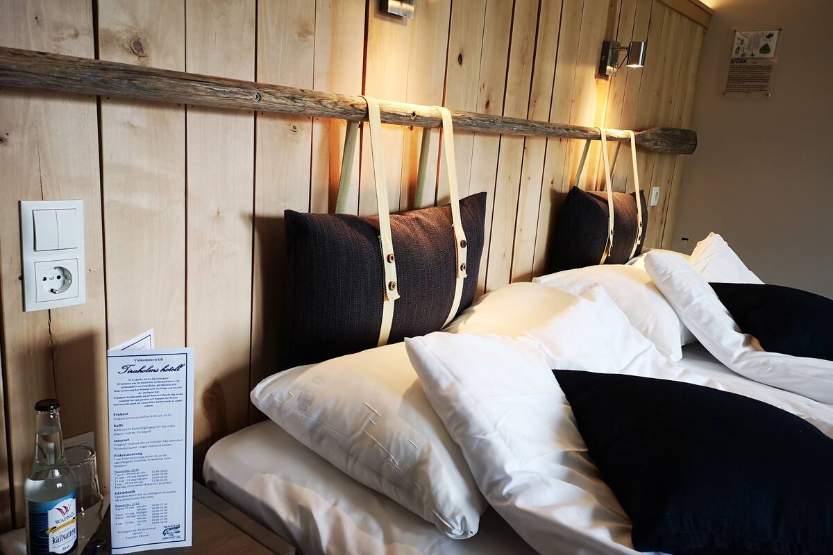 A wooden-paneled room with a bed, pillows, a menu, and a bottle of water.