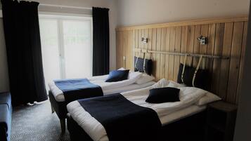 Een hotelkamer met twee bedden, een houten hoofdbord, een bankje en een raam met gordijnen.
