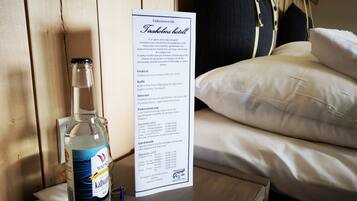 Quarto de hotel com parede de madeira, cama com roupa de cama branca, mesa de cabeceira com uma garrafa de Wapno Kålsvett e um menu na parede.